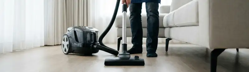 Professional house cleaner vacuuming a living room floor with a canister vacuum cleaner, Columbus, GA.