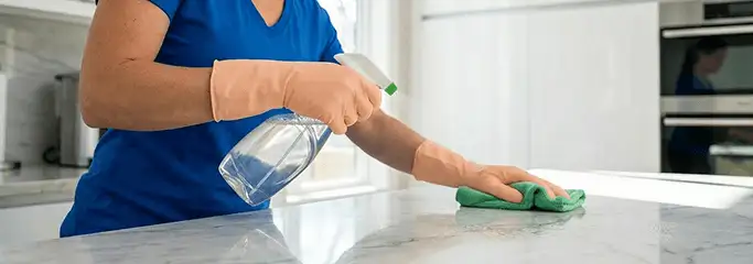 Maid service worker spraying and wiping a kitchen countertop with a microfiber cloth for sanitizing, Columbus, GA.