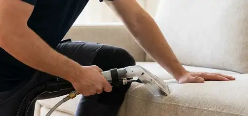 Professional upholstery cleaner deep-cleaning a fabric sofa with a handheld extraction tool, Columbus, GA.