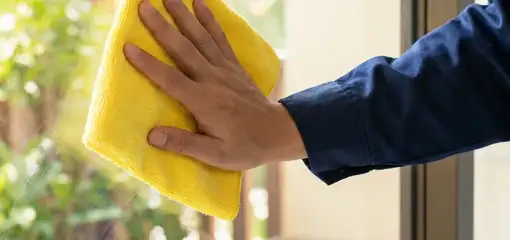 House cleaner wiping a glass window with a yellow microfiber cloth for streak-free cleaning, Columbus, GA.